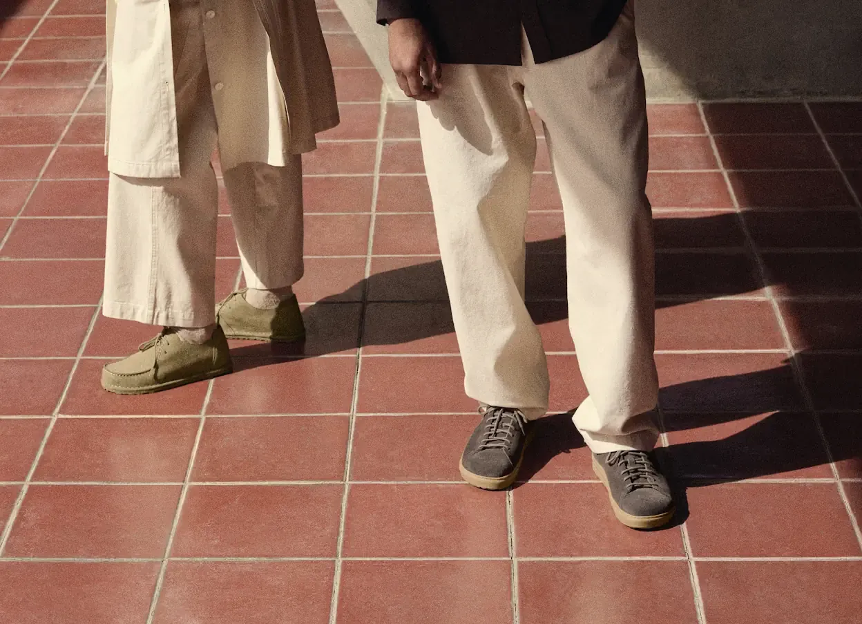 Dwie osoby prezentują jesienną stylizację na tle czerwonej, kwadratowej kostki brukowej. Jasne spodnie i płaszcz tworzą elegancki zestaw.