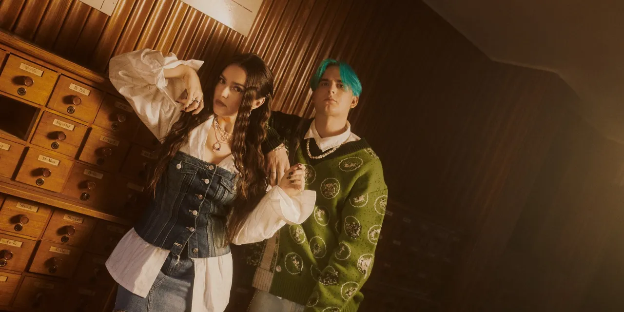 Para, kto śpiewa dzięki że jesteś, pozuje przy drewnianej szafie z szufladkami.