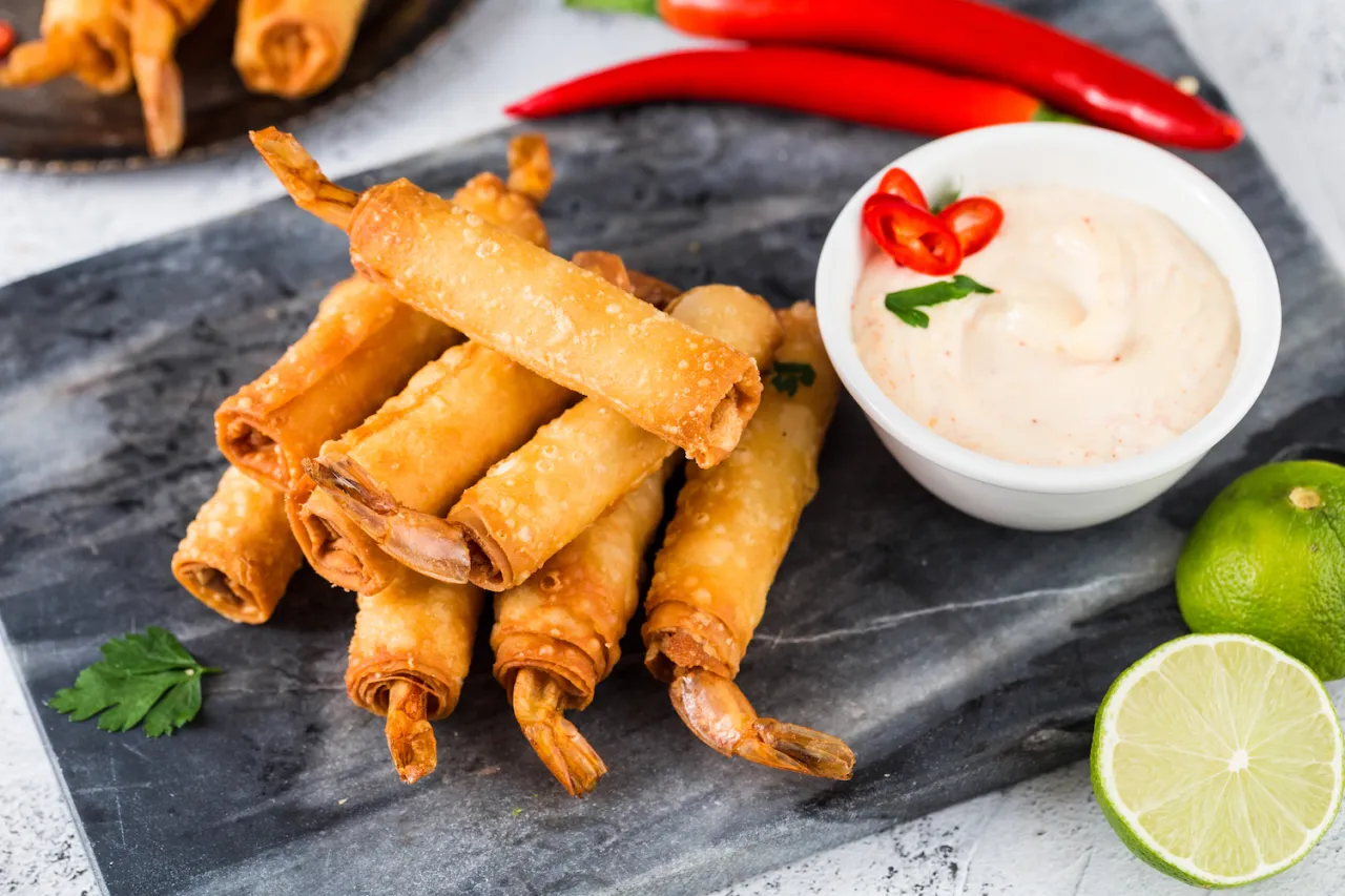 Chrupiące spring rolls z krewetkami, podane z dipem, limonką i papryczkami chili.