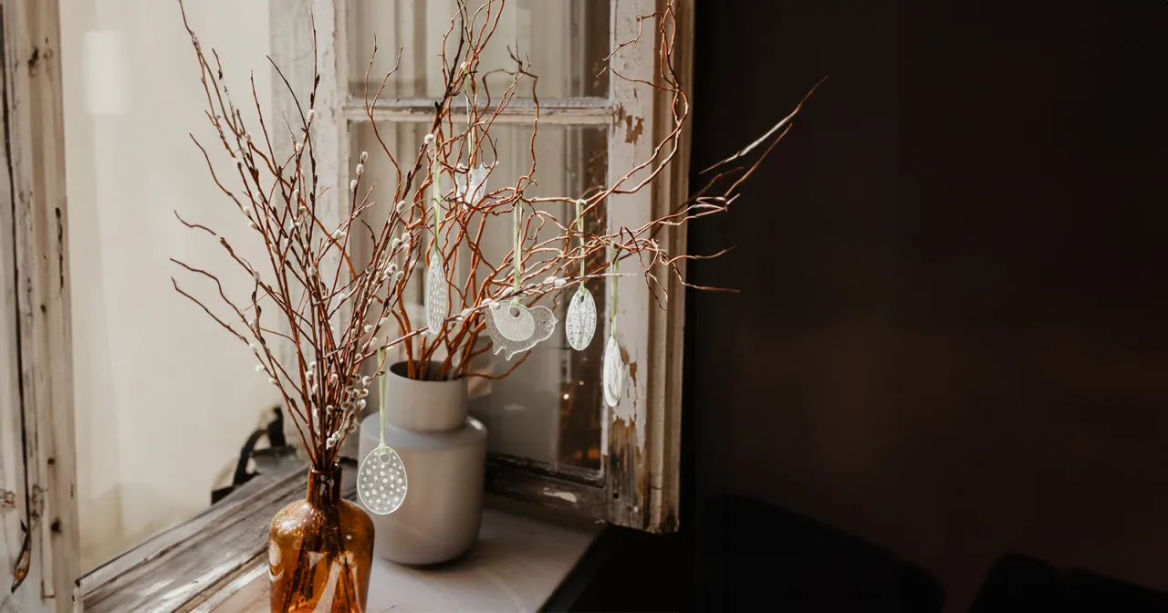 Nowoczesne, ręcznie robione stroiki wielkanocne z gałązek i ozdobnych jajek na tle starego okna.