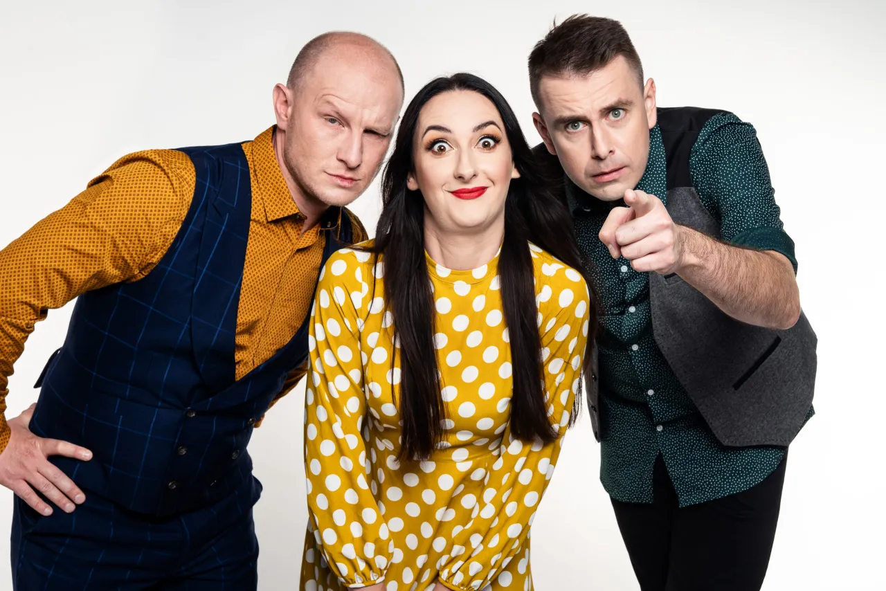Trzech artyst&oacute;w kabaretu K2 w zabawnych pozach. Kobieta w ż&oacute;łtej sukience w grochy, mężczyźni w kamizelkach.