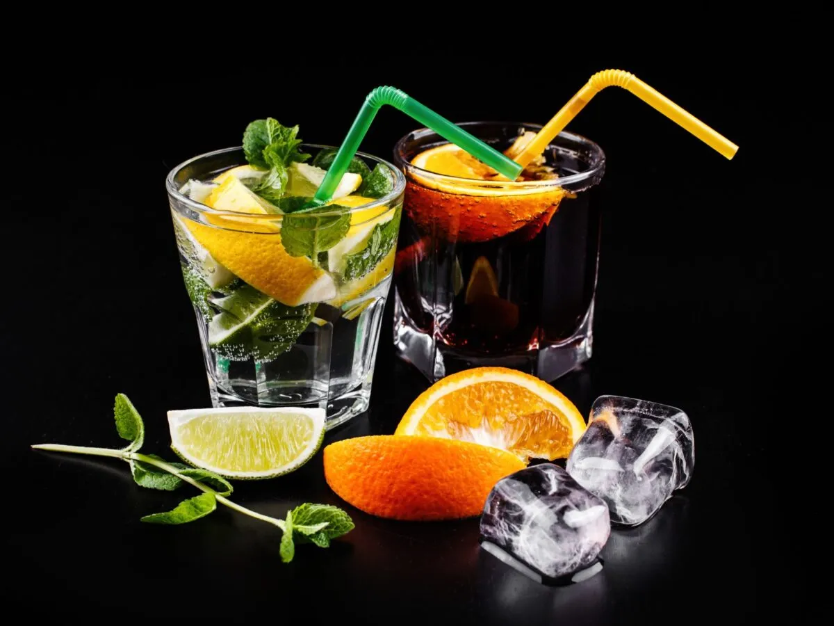 Orzeźwiający drink z kruszonym lodem i plasterkami cytryny, obok ciemny napój z pomarańczą.