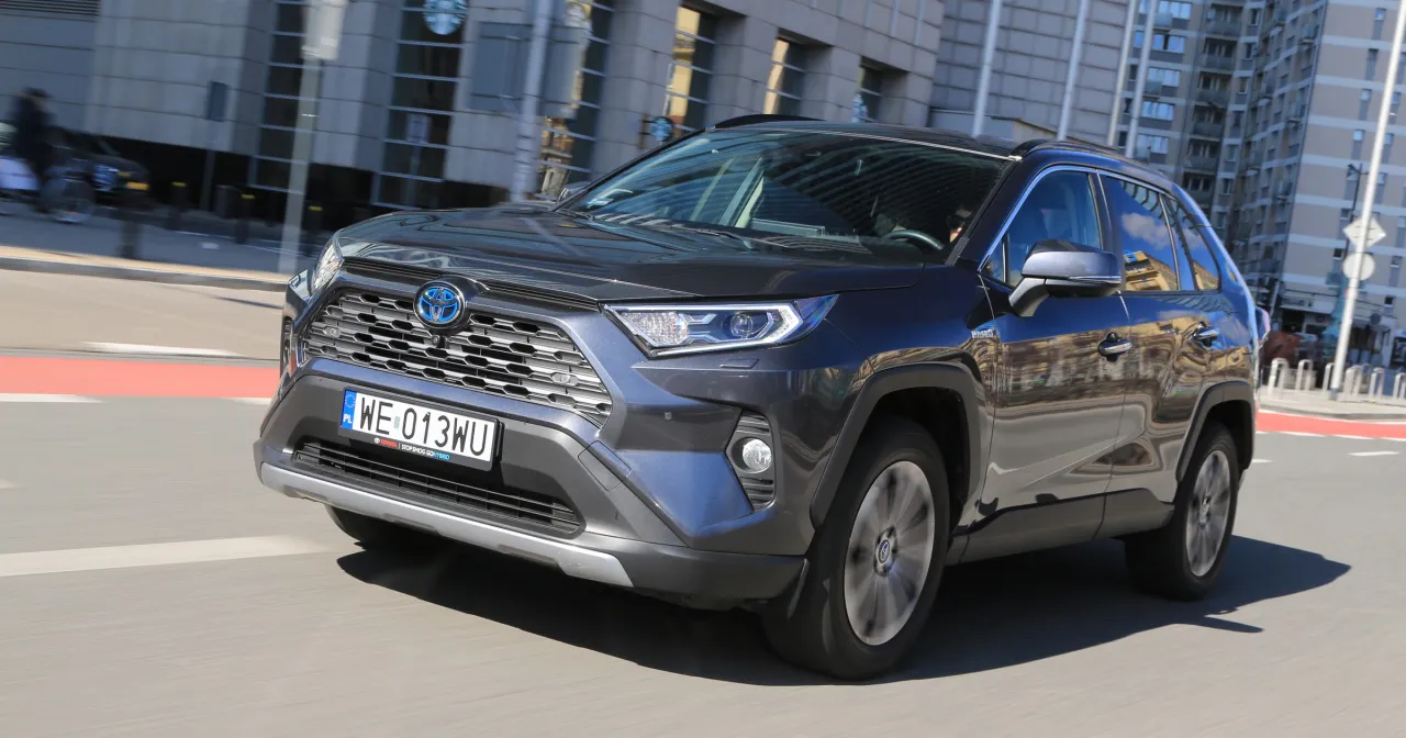 Szary Toyota RAV4 Hybrid w ruchu miejskim. Zastanawiasz się, ile kosztuje Toyota RAV4 Hybrid? Ten model to połączenie stylu i ekologii.