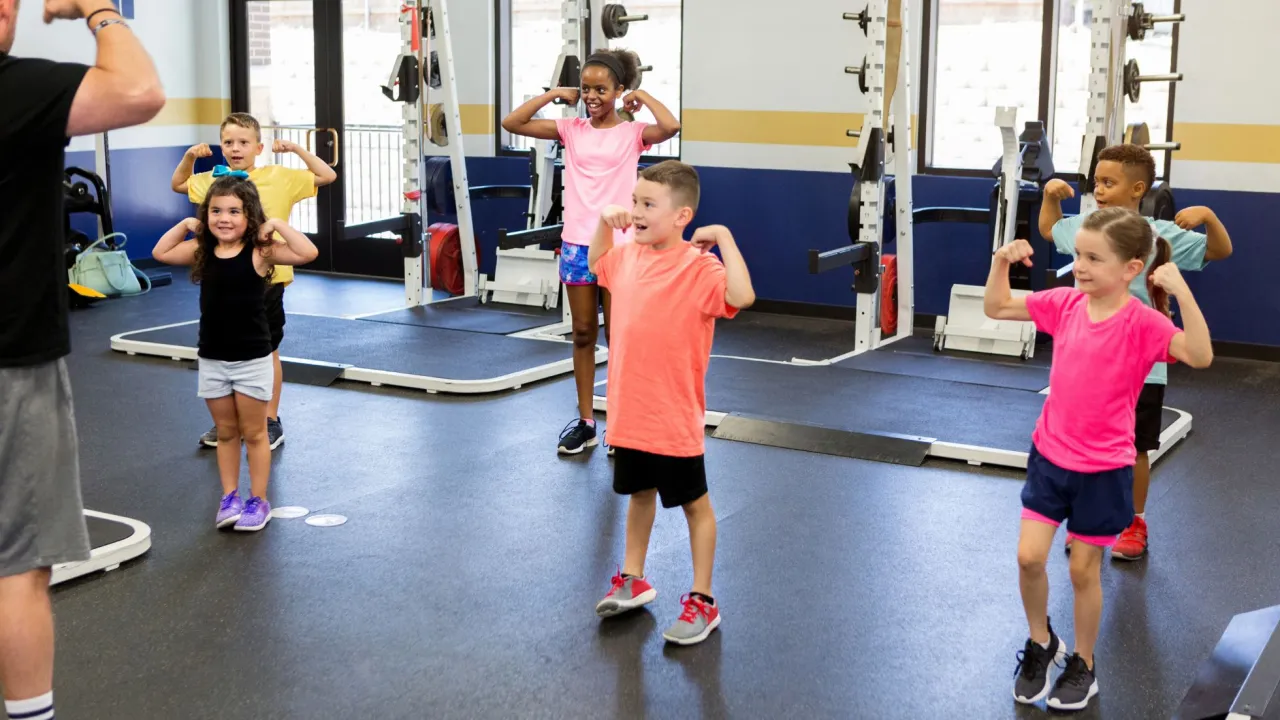 Dzieci ćwiczą w siłowni, pokazując bicepsy. To dowód, że crossfit dla kogo? Dla każdego, kto chce być silny!