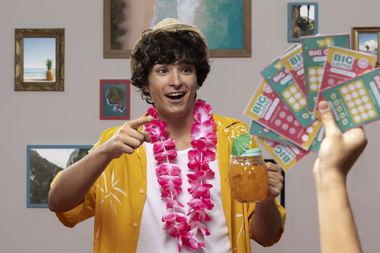 Chłopak w hawajskiej koszuli i z girlandą z kwiatów trzyma drinka i zdrapki Lotto. Czy na Orlenie są zdrapki Lotto?