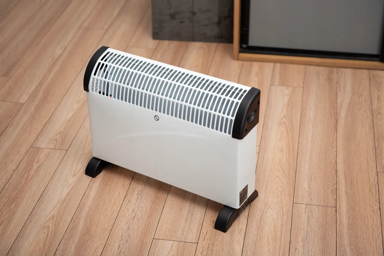 Biały grzejnik elektryczny na drewnianej podłodze. Szukasz odpowiedzi, jaki grzejnik elektryczny zużywa najmniej prądu?