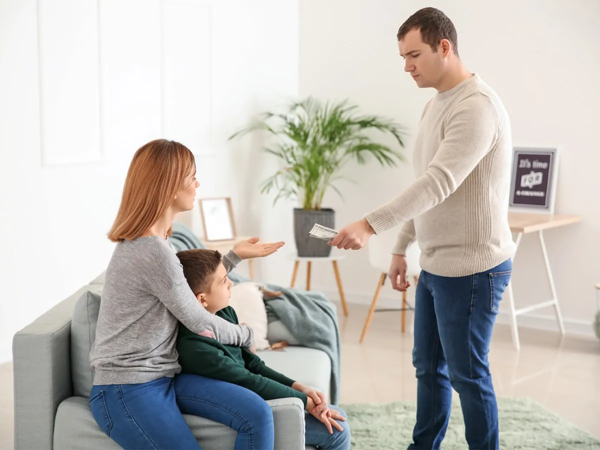 Kobieta z synem na kolanach gestykuluje, gdy ojciec wręcza jej pieniądze. Sytuacja przypomina moment, gdy matka zostawia dziecko ojcu.