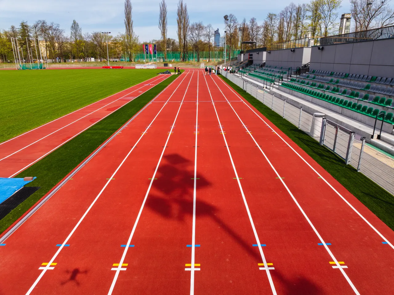 Czerwona bieżnia stadionu z zieloną murawą. Widać trybuny i kilka osób. Standardowa bieżnia ma 400 metrów.