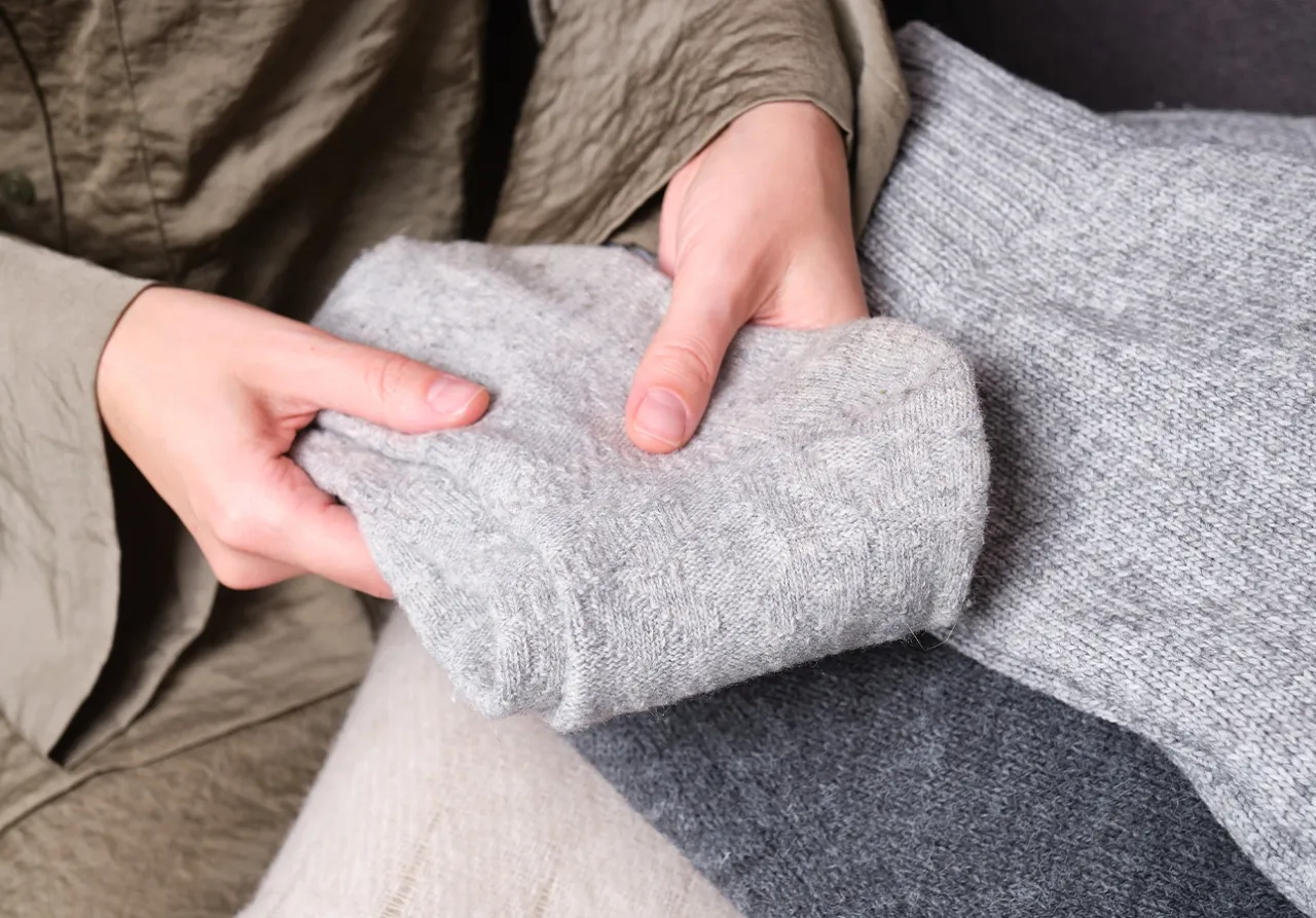 Delikatne dłonie trzymają szary, kaszmirowy sweter, pokazując jego fakturę. Dowiedz się, jak prać kaszmirowy sweter, by zachować jego miękkość.