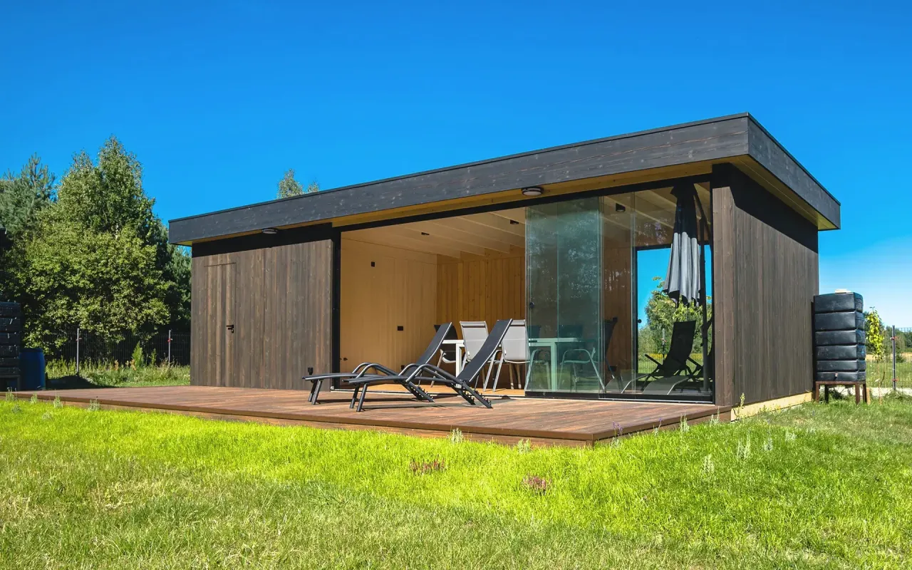 Nowoczesna altana z drewnianą zabudową i przeszklonymi ścianami. Idealne miejsce, by odpocząć i zastanowić się, czym zabudować altanę, by była funkcjonalna.