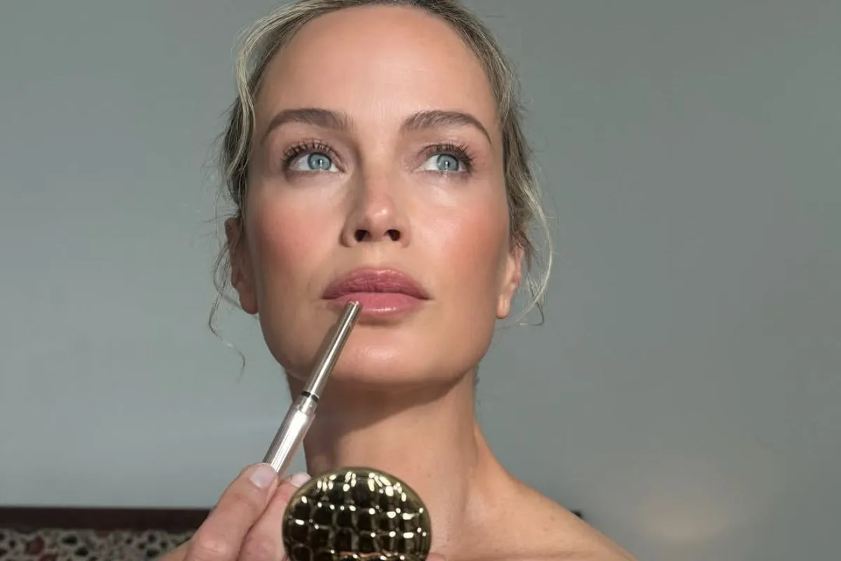 Delikatny makijaż dla 50 latki. Kobieta z błękitnymi oczami podkreśla usta konturówką.