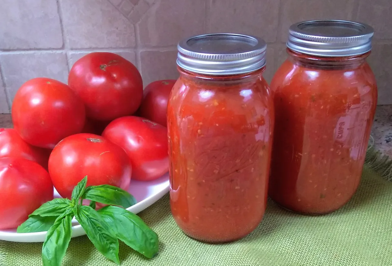 Słoiki z domowym sosem pomidorowym, idealnym do spaghetti. Obok świeże pomidory i bazylia &ndash; klucz do tego, jak zrobić sos do spaghetti z pomidor&oacute;w.