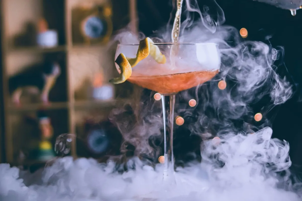 Dymiący drink przepis: koktajl w kieliszku z pomarańczową skórką, otoczony mgłą.