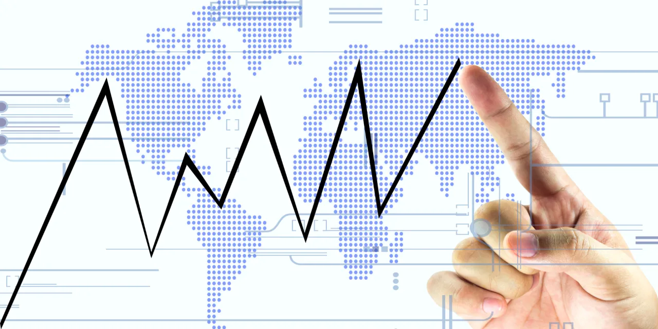 Wykres giełdowy na tle mapy świata. Palec wskazuje na wykres, sugerując analizę danych i moment, o kt&oacute;rej otwiera się giełda w USA.