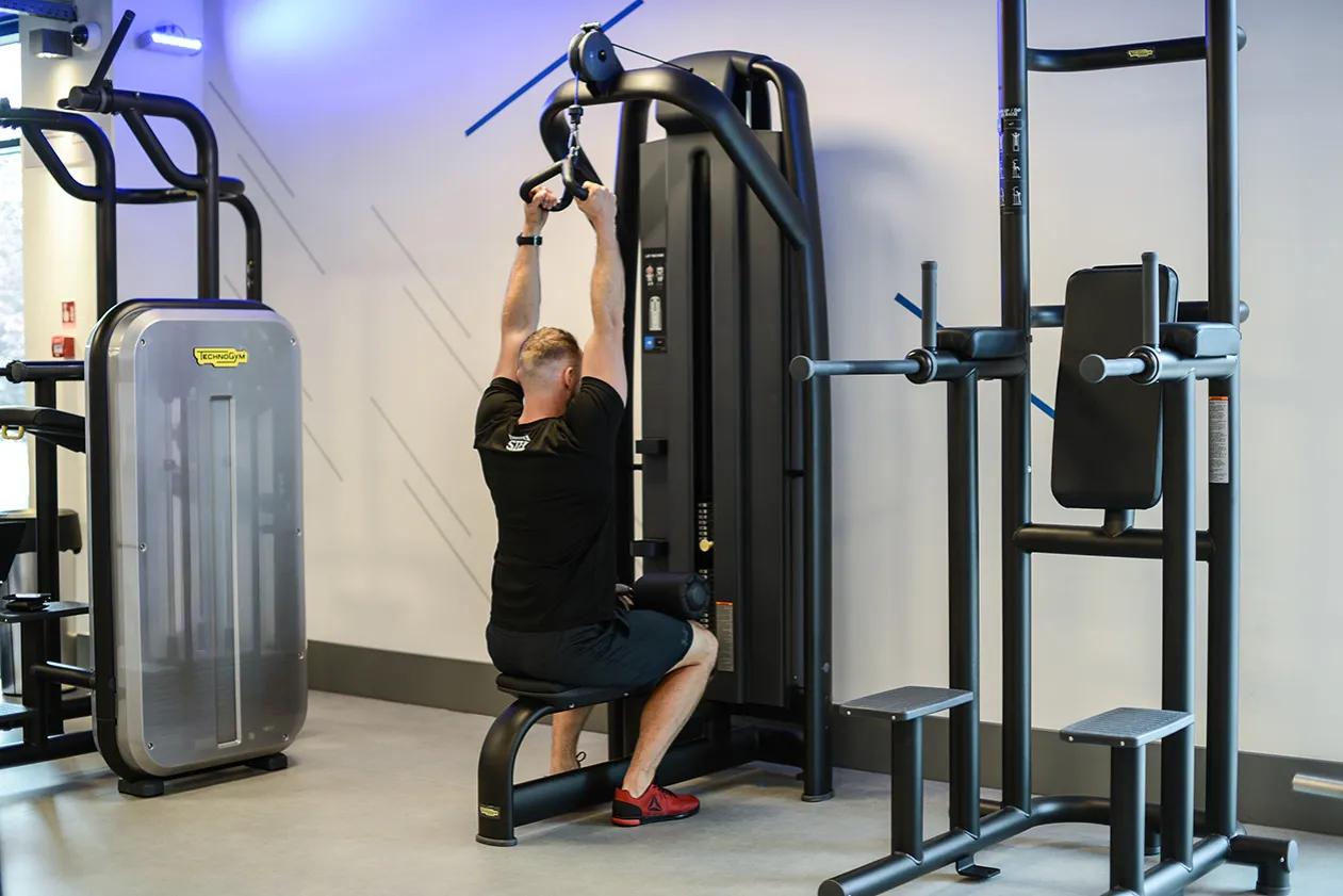 Mężczyzna wykonuje ćwiczenia na wyciągu g&oacute;rnym, trenując mięśnie plec&oacute;w. To świetny spos&oacute;b na budowanie siły.
