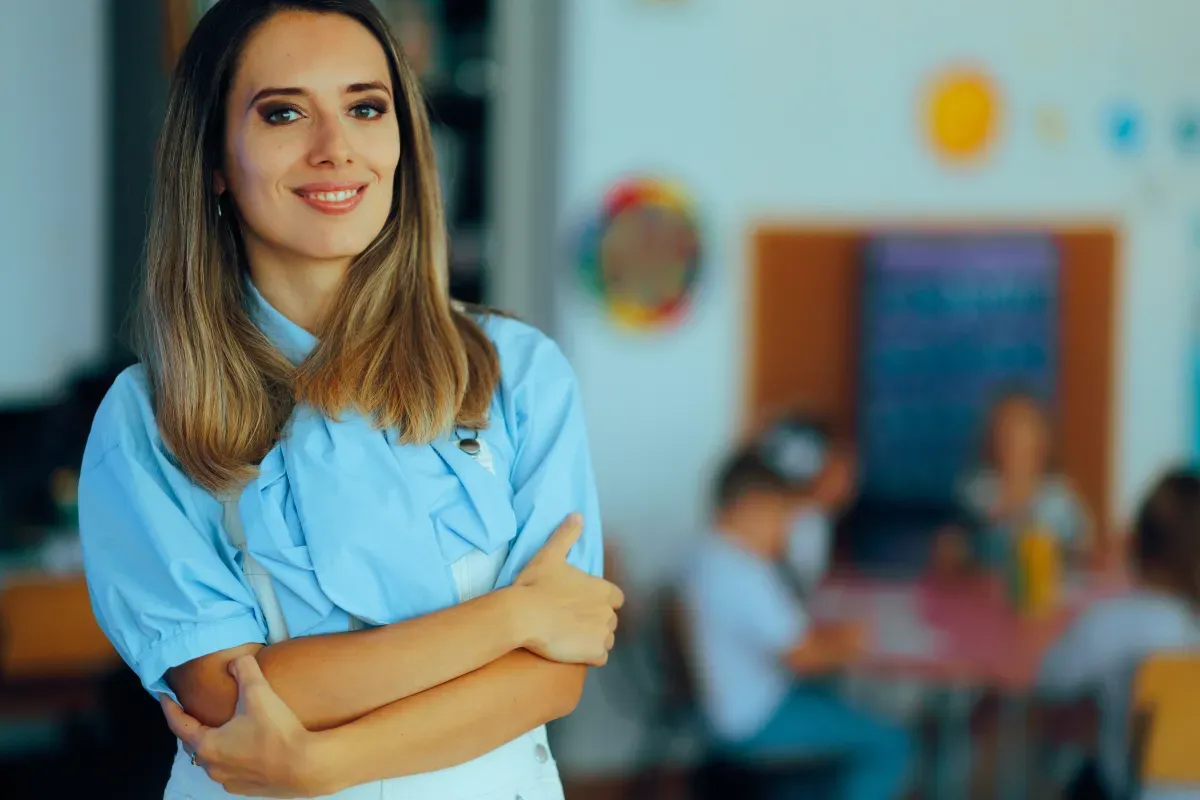Uśmiechnięta nauczycielka w jasnym pokoju, inspirująca do tego, jak zdobyć uprawnienia pedagogiczne. Dzieci w tle.