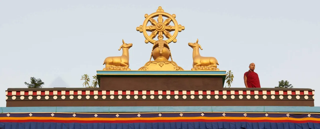 Złote koło Dharmy i jelenie na dachu świątyni, gdzie dominuje buddyzm. Mnich w czerwonej szacie.