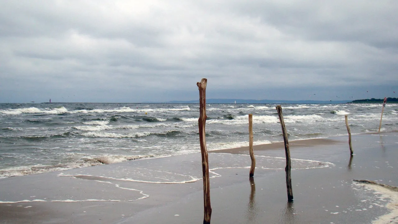 Mroczne chmury nad Bałtykiem, fale rozbijają się o brzeg, a drewniane pale stoją samotnie, gdy sztorm na Bałtyku nabiera sił.