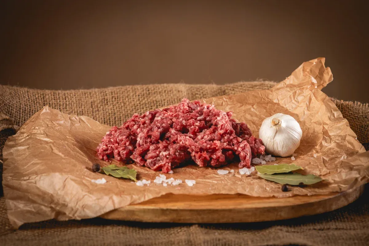 Świeże, mielone mięso wołowe, idealne na soczyste burgery. Obok czosnek, liście laurowe i sól.