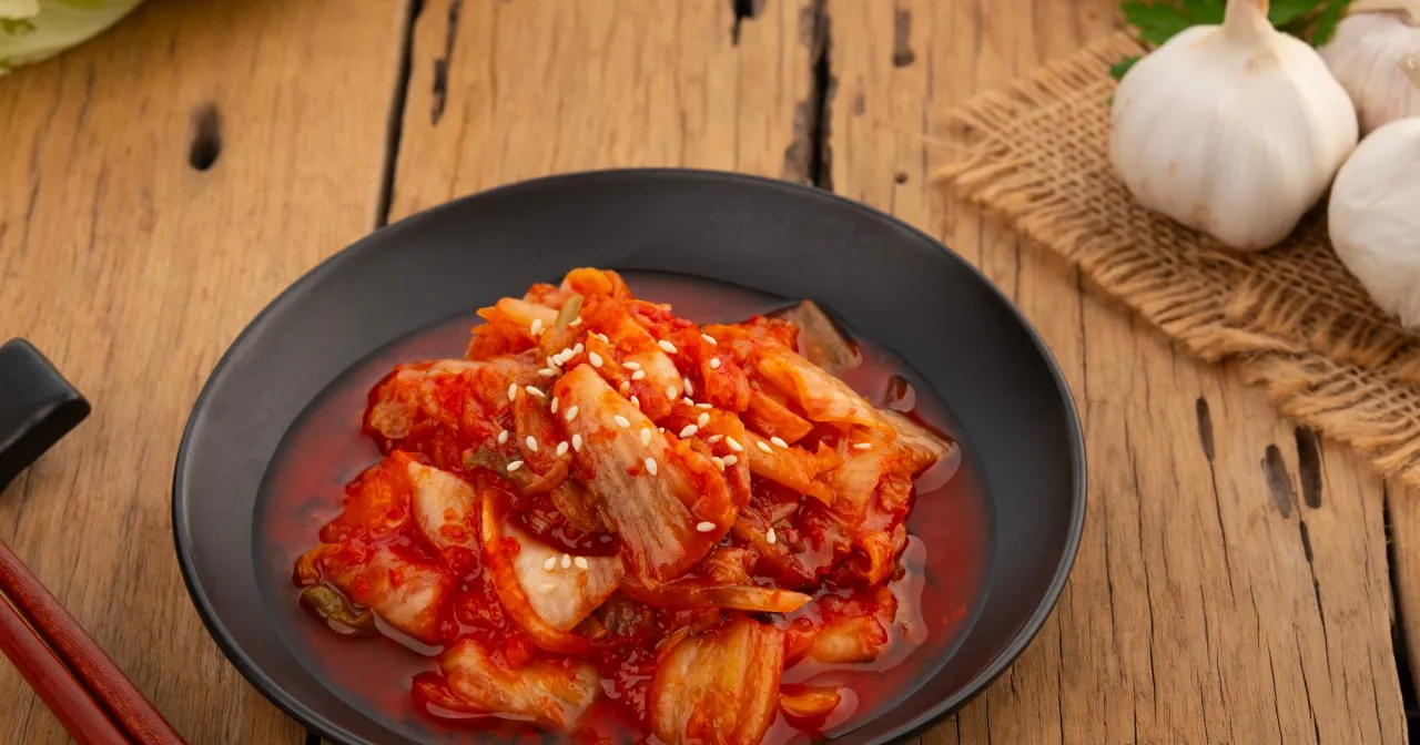 Pikantna kapusta kimchi co to jest? Fermentowana, czerwona kapusta z sezamem na czarnym talerzu, obok czosnku i pałeczek.