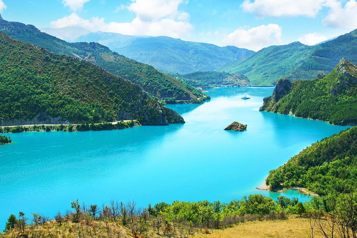 Turkusowe jezioro otoczone zielonymi wzg&oacute;rzami, ł&oacute;dź na wodzie. Jedno z najpiękniejszych miejsc we Francji.