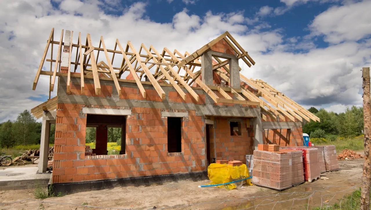 Budowa domu w toku: ściany z cegły, drewniany szkielet dachu i materiały budowlane czekają na dalsze prace.