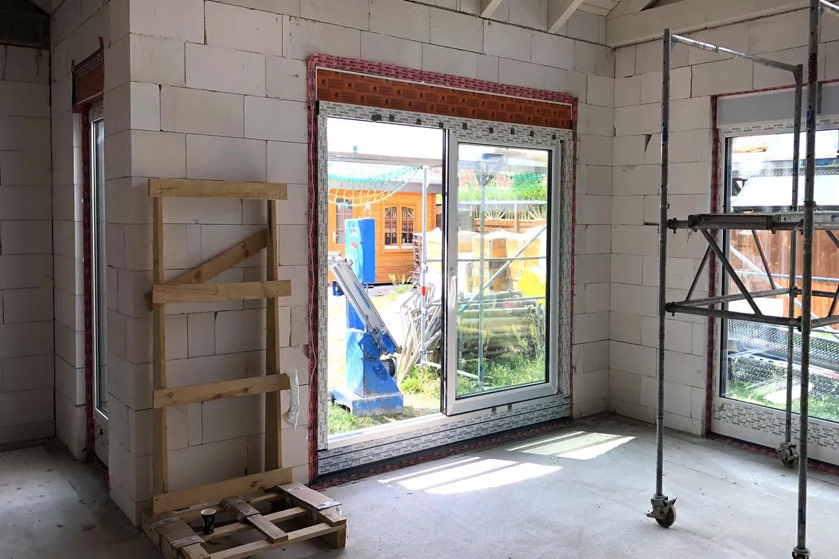 Wnętrze domu w budowie, widoczne okna z taśmą izolacyjną, gotowe do ciepły montaż po zamontowaniu okien.