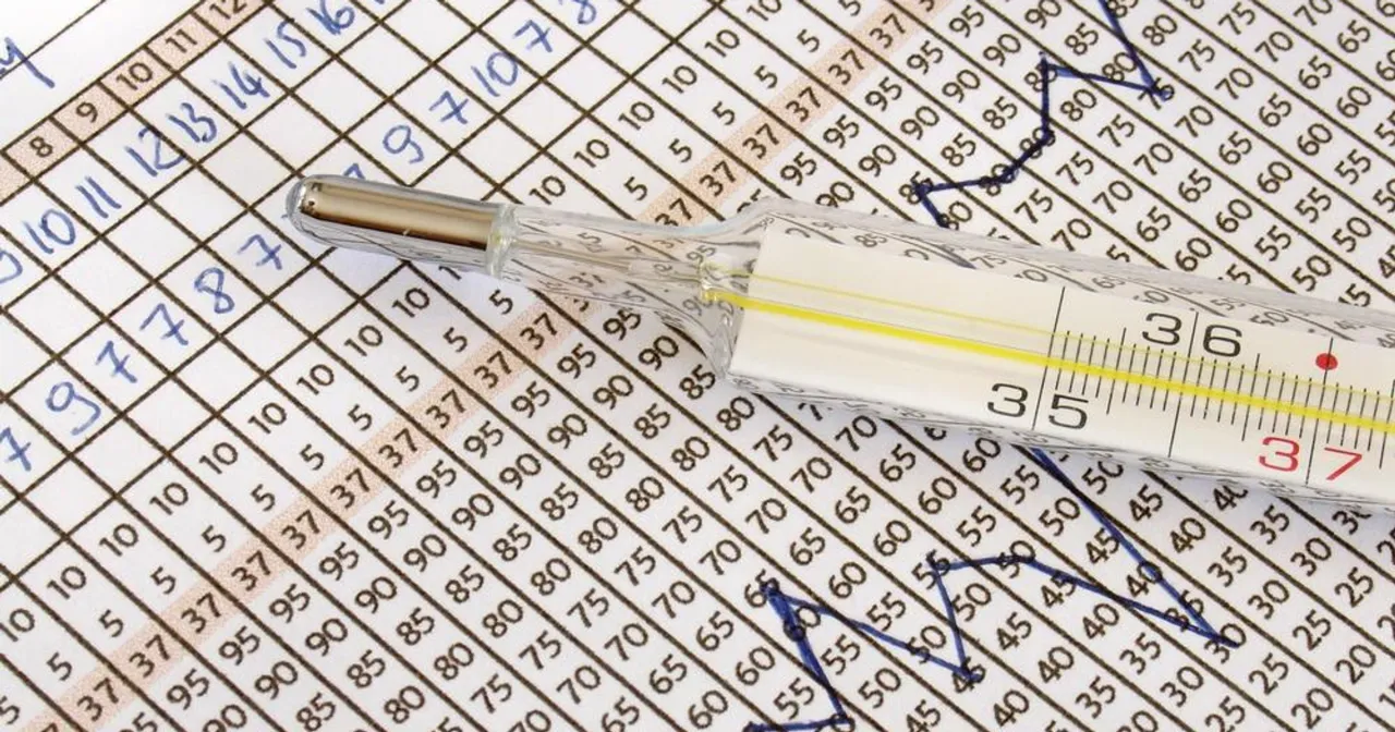 Termometr lekarski na tle wykresu i tabeli z danymi. Wskazuje temperaturę ok. 37°C. To może być pomocne przy ustalaniu, kiedy najlepiej badać progesteron.