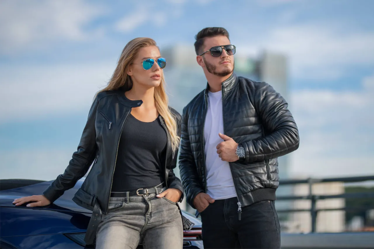 Para kurtki skórzanej idealne są jeansy. Para młodych ludzi w skórzanych kurtkach i okularach przeciwsłonecznych pozuje przy samochodzie.