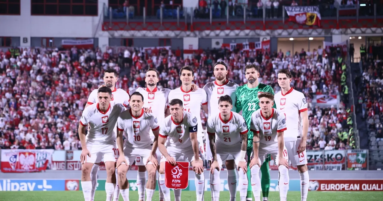 Piłkarze reprezentacji Polski w białych strojach, gotowi do gry. Tłum kibic&oacute;w na trybunach w biało-czerwonych barwach.