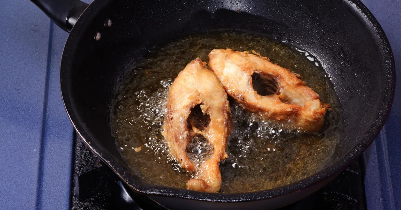 Dwa kawałki ryby smażą się na głębokim oleju w czarnej patelni. Idealny sposób, na czym smażyć rybę, by była chrupiąca.