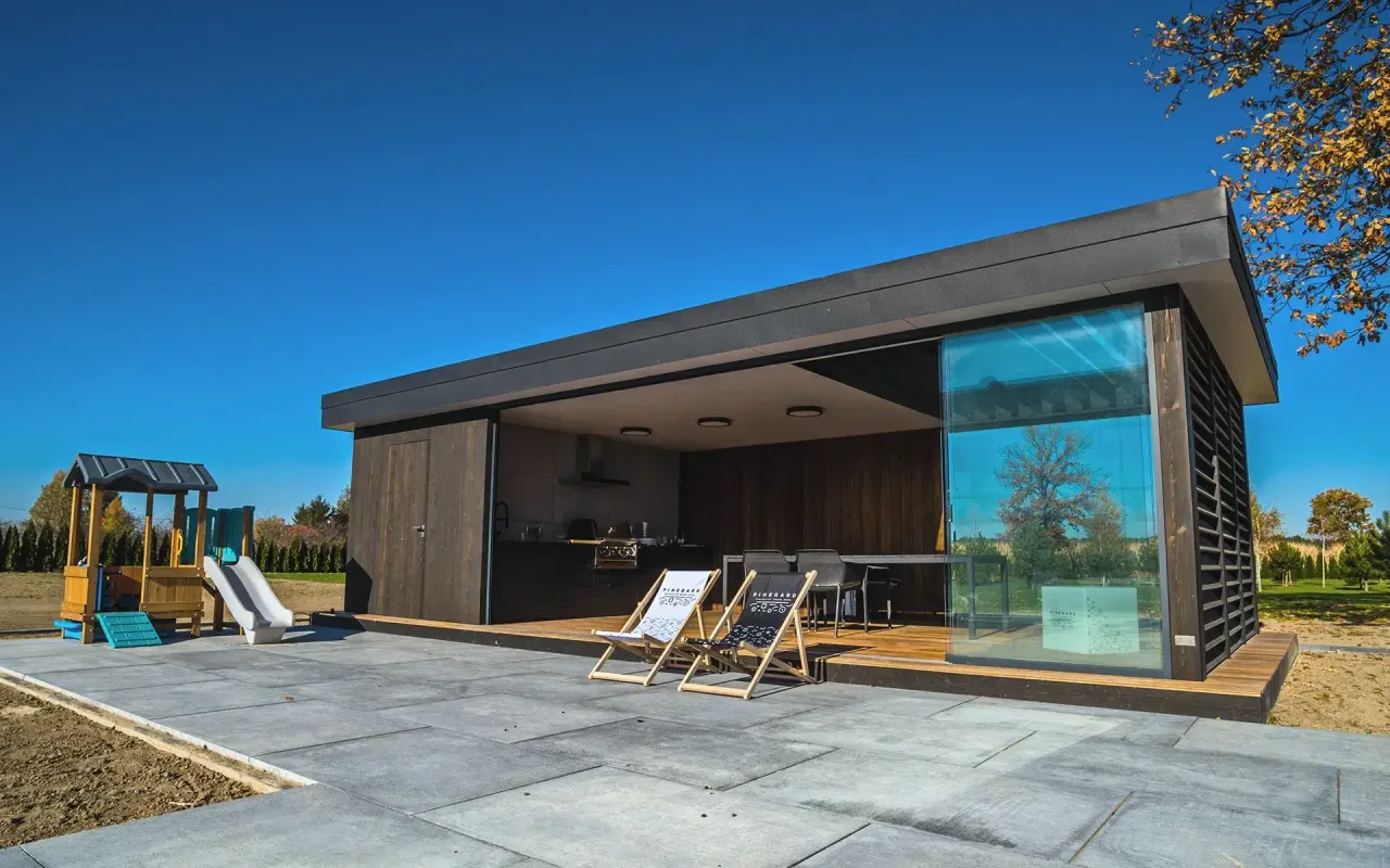 Nowoczesna altana ogrodowa z kuchnią i miejscem do wypoczynku. Obok plac zabaw dla dzieci.