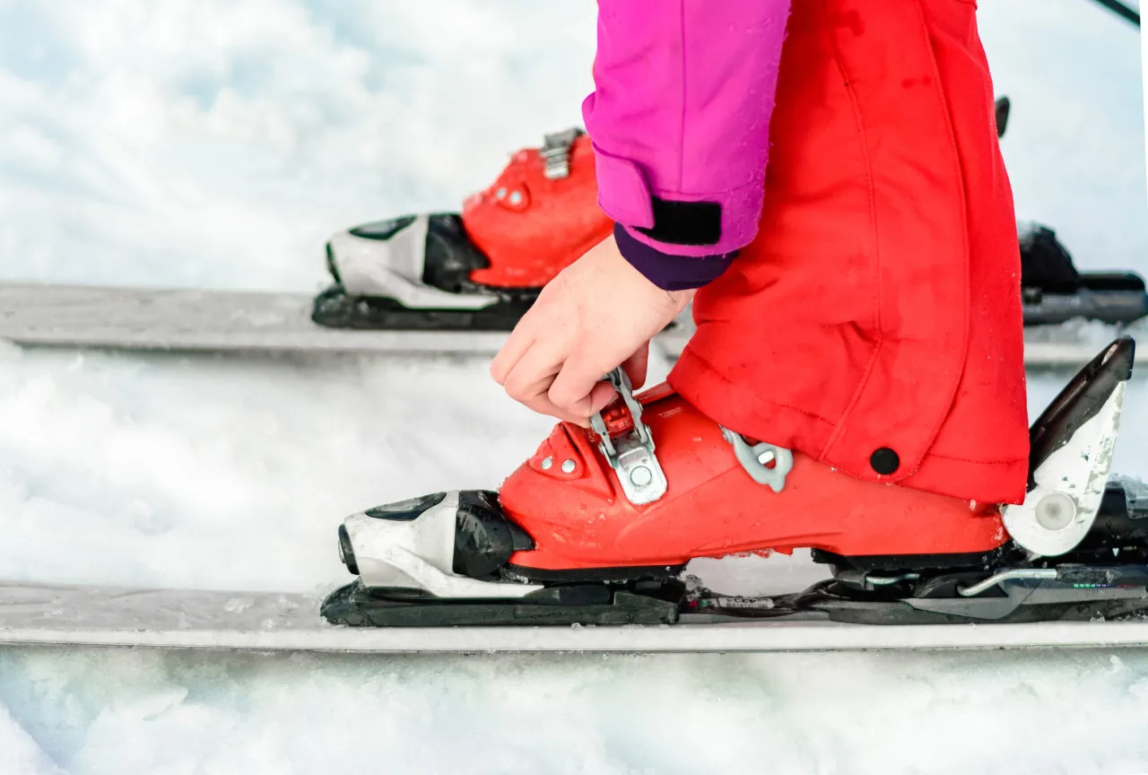 Dłoń zapina klamrę czerwonego buta narciarskiego, przygotowując się do jazdy. To kluczowy moment, by wiedzieć, jak ustawić DIN w nartach dla bezpieczeństwa.