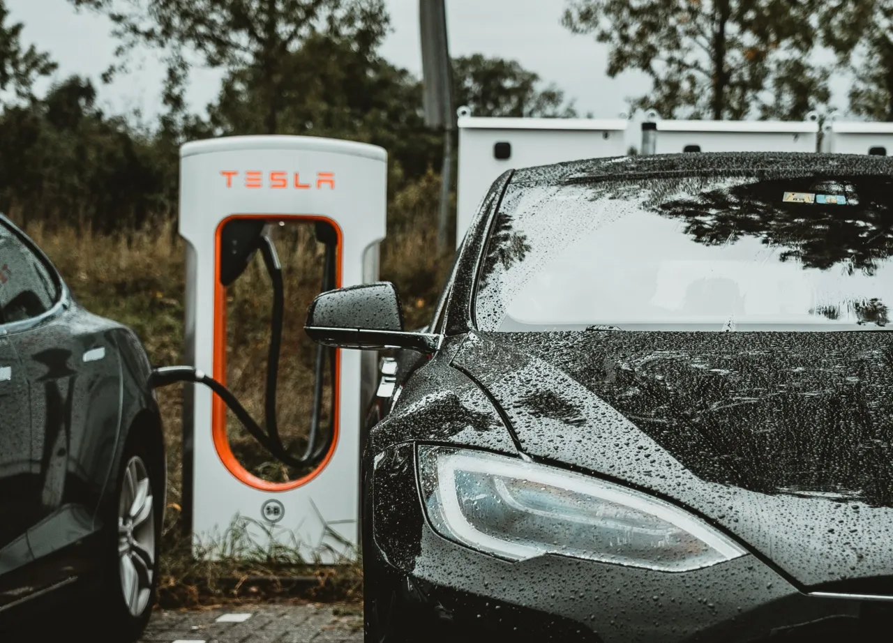 Czarna Tesla na deszczu pod ładowarką. Zastanawiasz się, jak długo ładuje się Tesla?