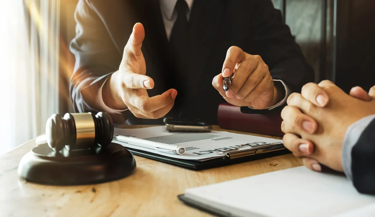 Prawnik omawia umowę, a obok młotek sędziowski. Czy adwokat z urzędu jest płatny? Rozmowa o kosztach pomocy prawnej.