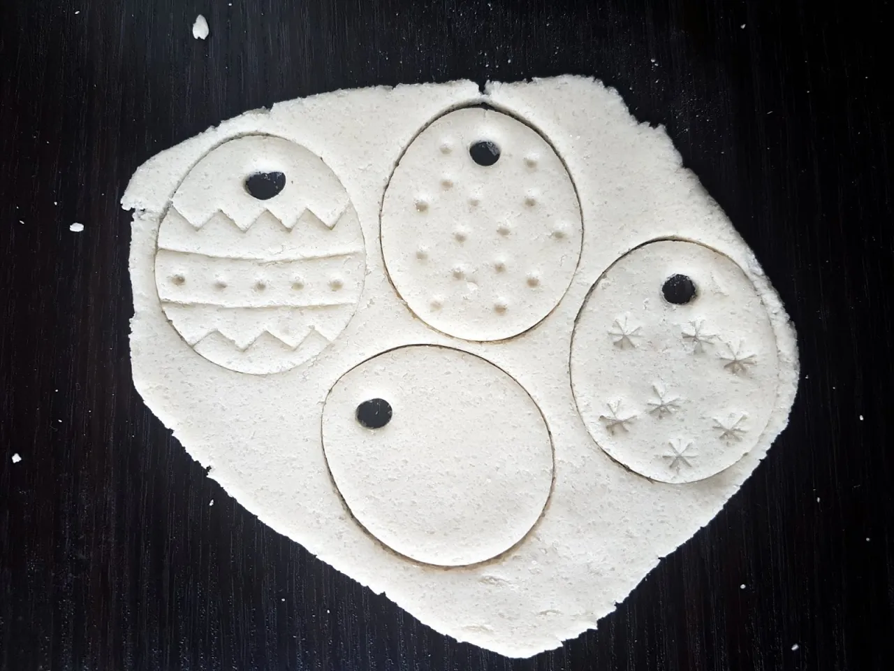 Wytrawne ozdoby wielkanocne robione przez dzieci. Jajka z ciasta z wzorami i otworami na sznurek.