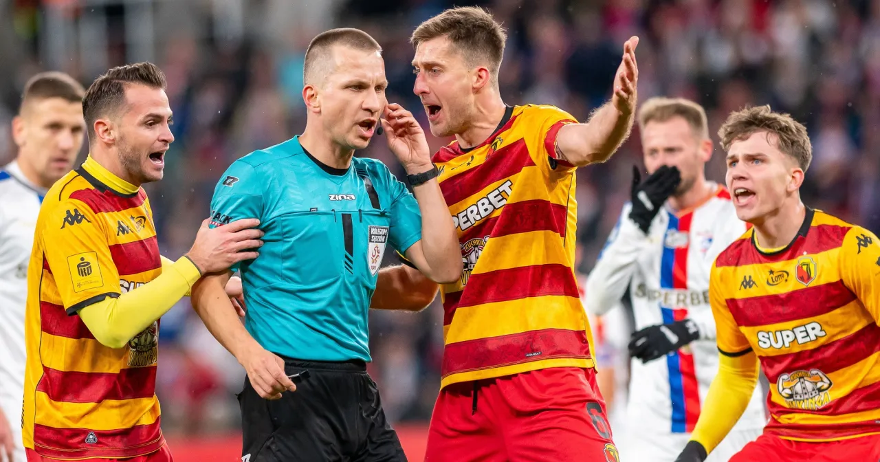 Piłkarze w żółto-czerwonych strojach dyskutują z sędzią. Emocje sięgają zenitu, jakby to był ostatni mecz ekstraklasy.