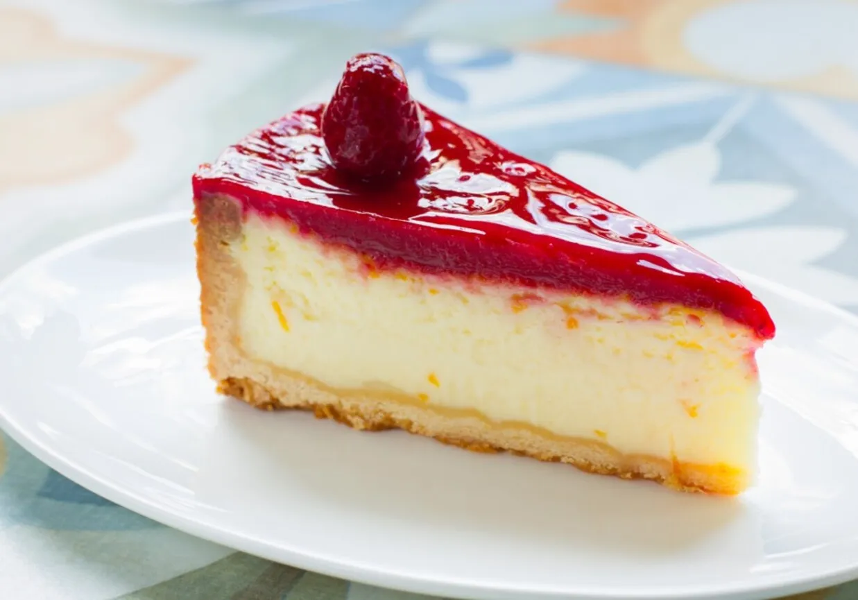 Pyszny sernik na zimno z malinową polewą i maliną na wierzchu, na kruchym spodzie. Idealny wybór na deser!