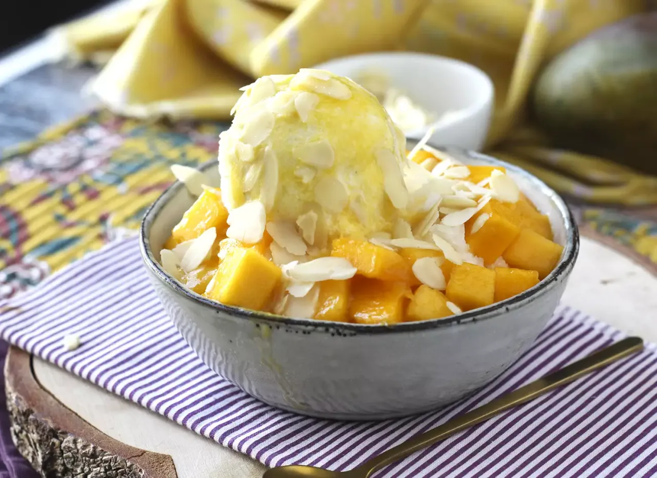 Pyszny deser Bingsu przepis: kostki mango, gałka lodów i płatki migdałów w miseczce.