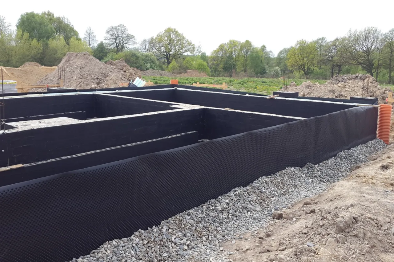 Fundament pod domek narzędziowy w trakcie budowy. Widoczne izolowane ściany fundamentowe i podsypka żwirowa.