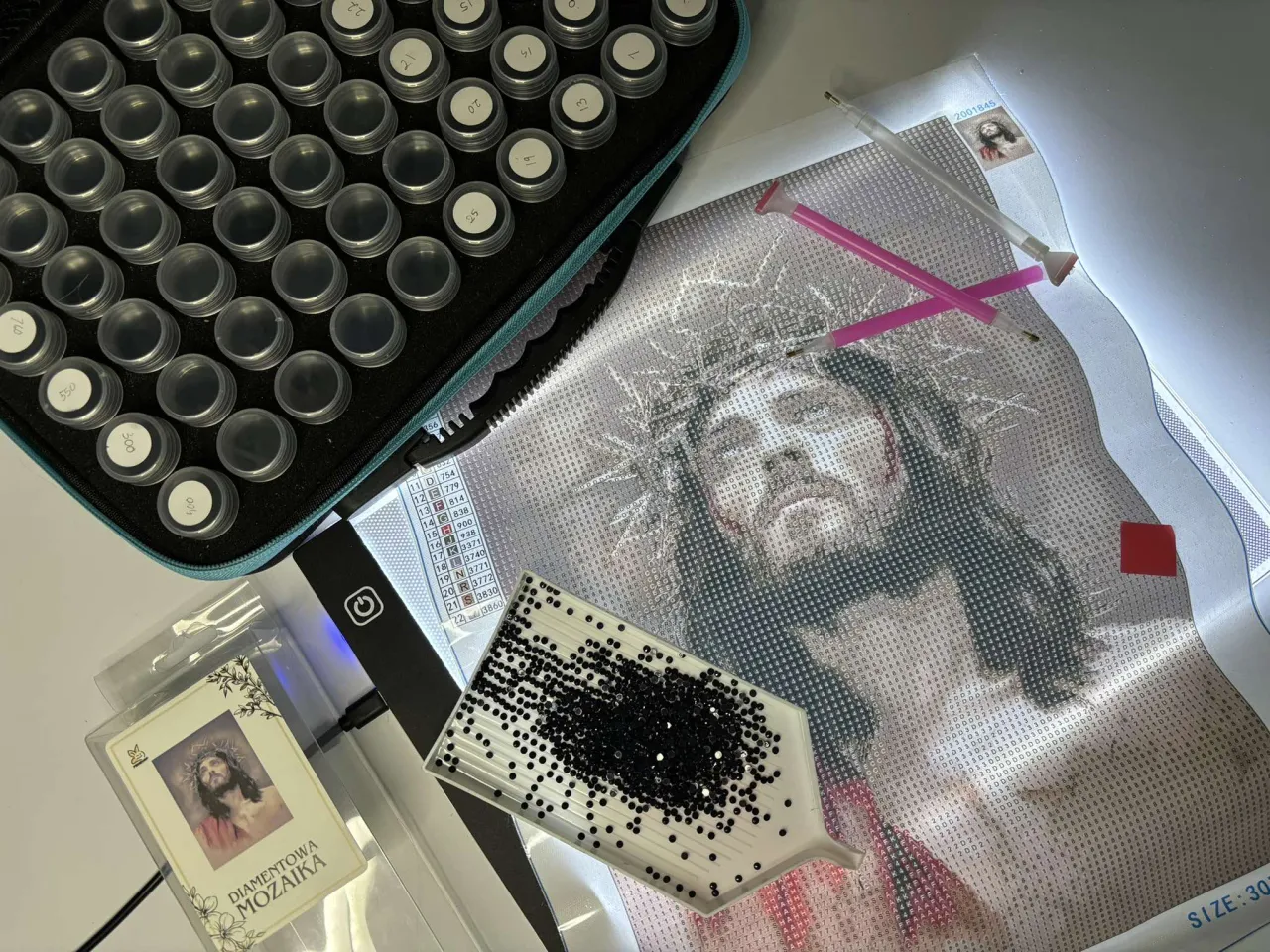 Zestaw do haftu diamentowego: pł&oacute;tno z wizerunkiem Jezusa, pojemniczki z diamencikami, tacka i pisaki. Jak zrobić haft diamentowy?