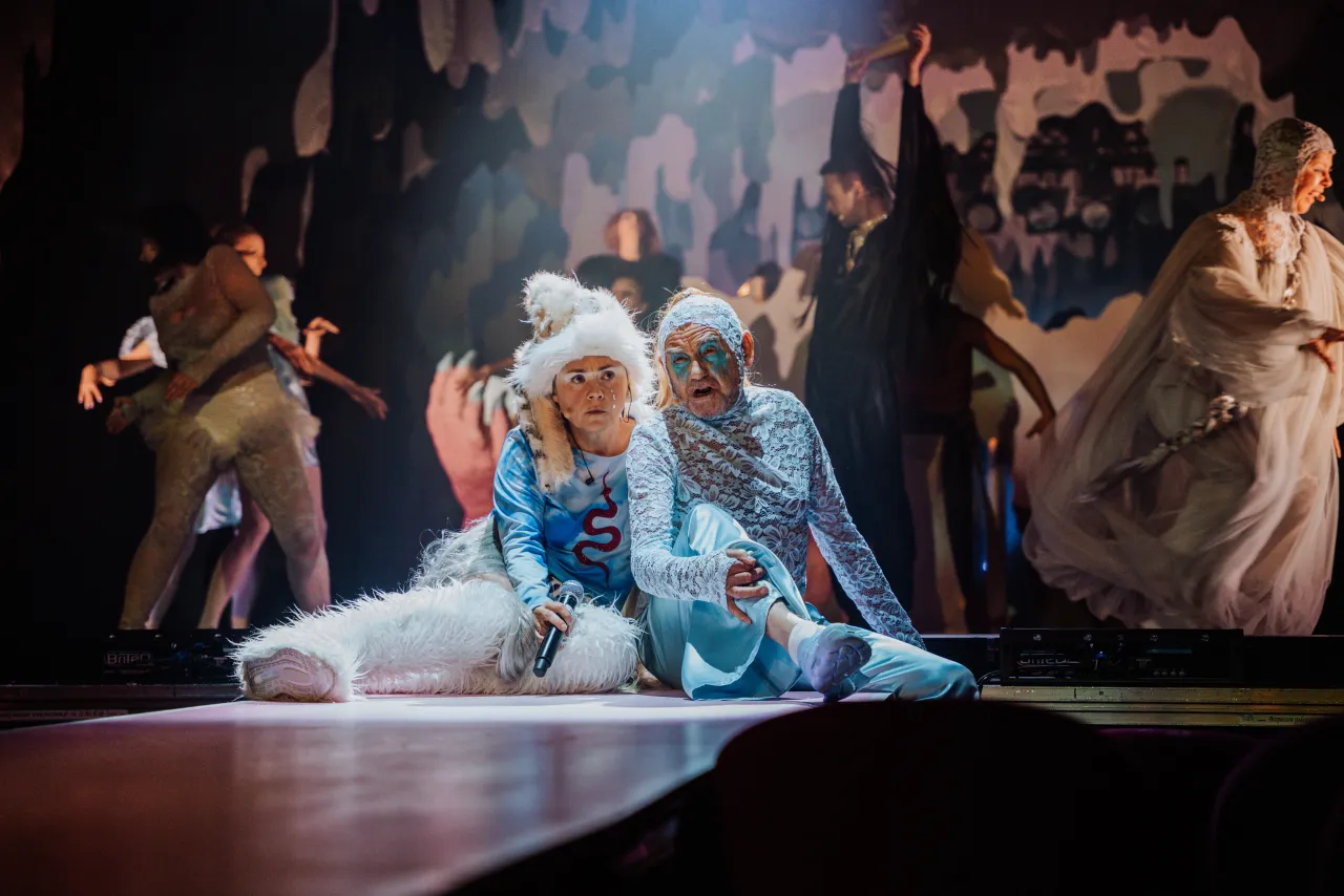 Dwie postacie w fantazyjnych strojach siedzą na scenie, przygotowując się do jednego z najlepszych spektakli teatralnych.