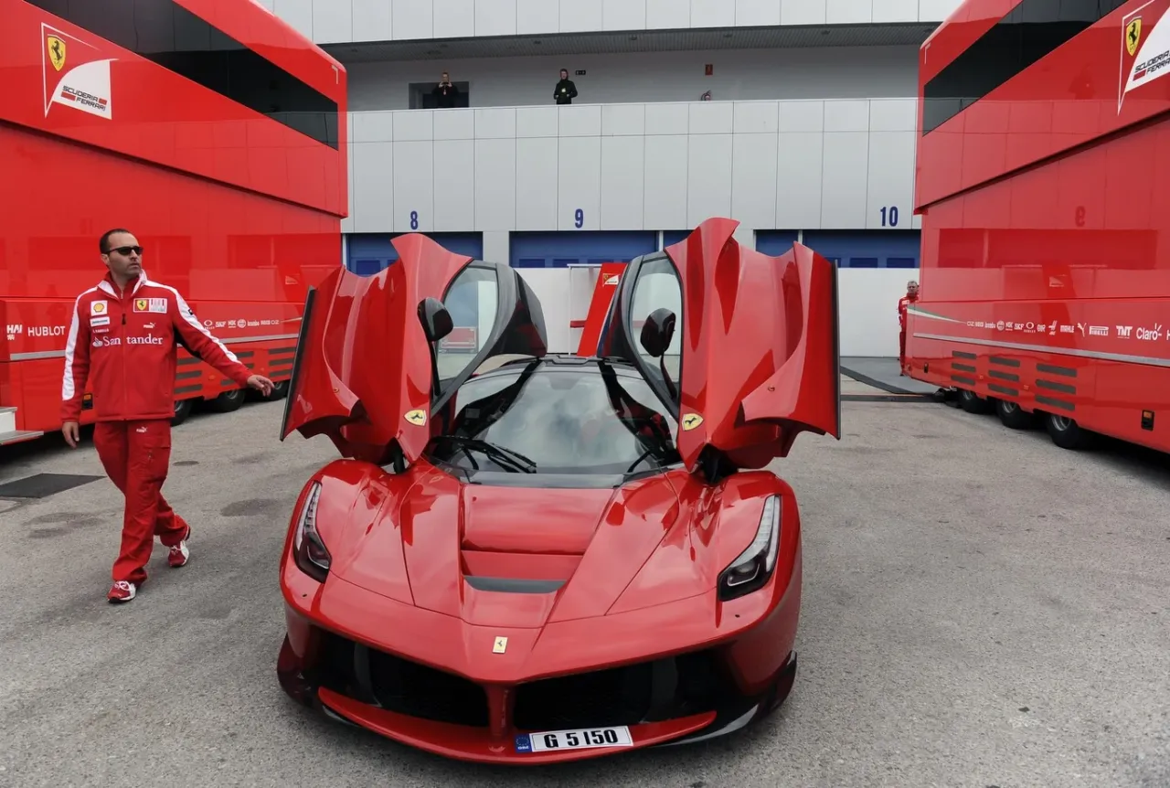 Czerwone Ferrari LaFerrari z otwartymi drzwiami, obok czerwony bus. Zastanawiasz się, ile kosztuje Ferrari LaFerrari?