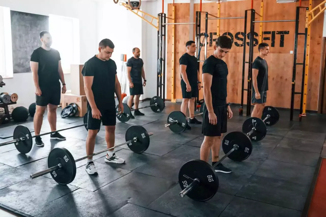 Mężczyźni w czarnych strojach ćwiczą z ciężarami. Czy to crossfit czy siłownia? Wygląda na intensywny trening.