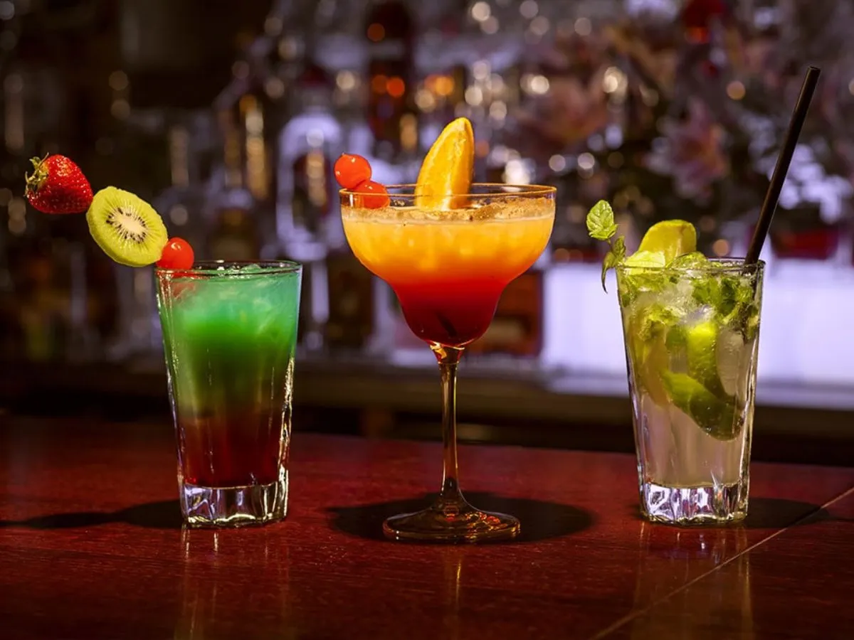 Trzy kolorowe drinki na barze: zielony z owocami, pomarańczowo-czerwony w kieliszku oraz mojito. Idealne na letnie popołudnie, może nawet z dodatkiem Fanta.