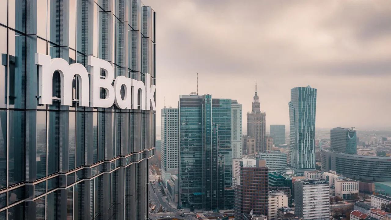 Logo mBank na szklanym wieżowcu w centrum miasta. W tle panorama Warszawy z Pałacem Kultury. Planujesz jak spłacić kredyt odnawialny mbank?