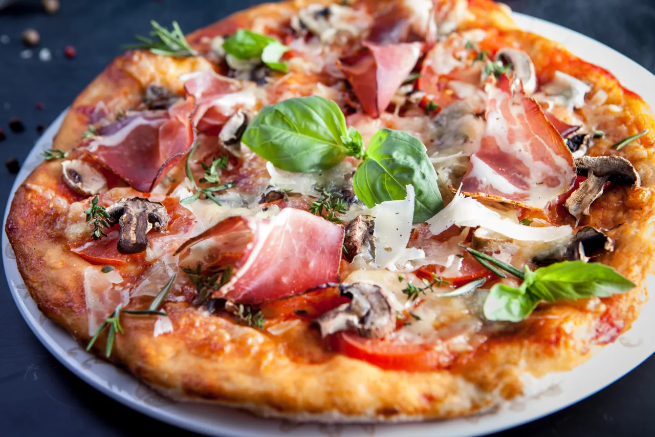 Domowa pizza z prosciutto, pieczarkami, pomidorami i bazylią. Idealna na rodzinny obiad.
