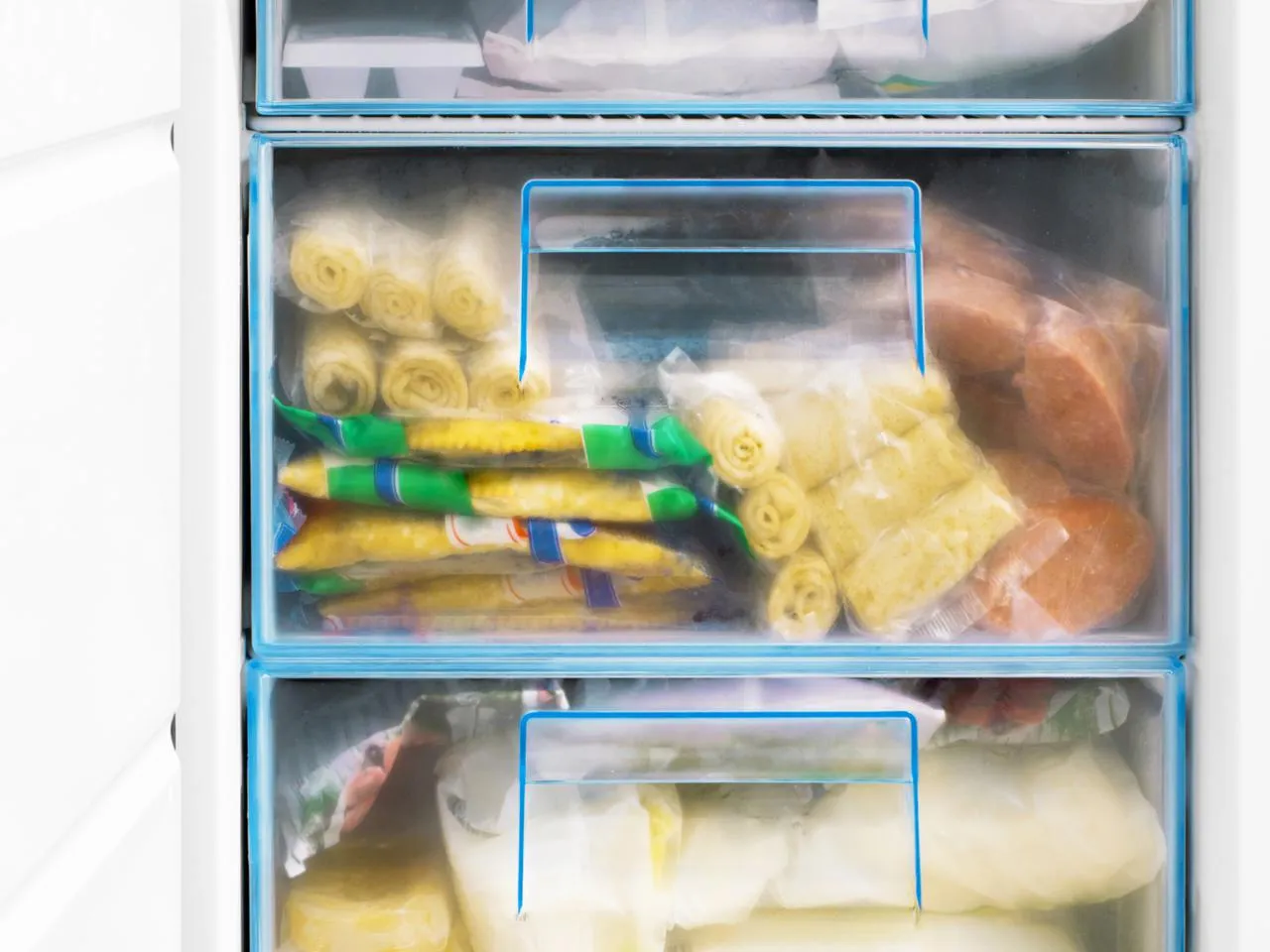 Zamrożone warzywa w szufladach zamrażarki. Widać mrożone fasolki, kukurydzę, a także inne produkty, kt&oacute;re można mrozić.