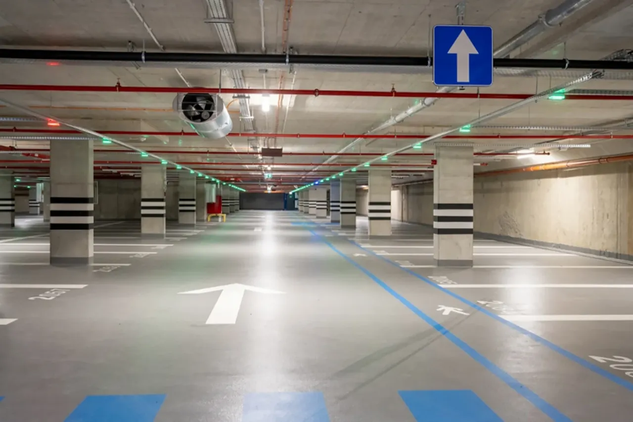 Pusta hala garażowa z wyznaczonymi miejscami parkingowymi i strzałkami na podłodze. Idealne miejsce, gdzie można poćwiczyć jazdę samochodem w Warszawie.