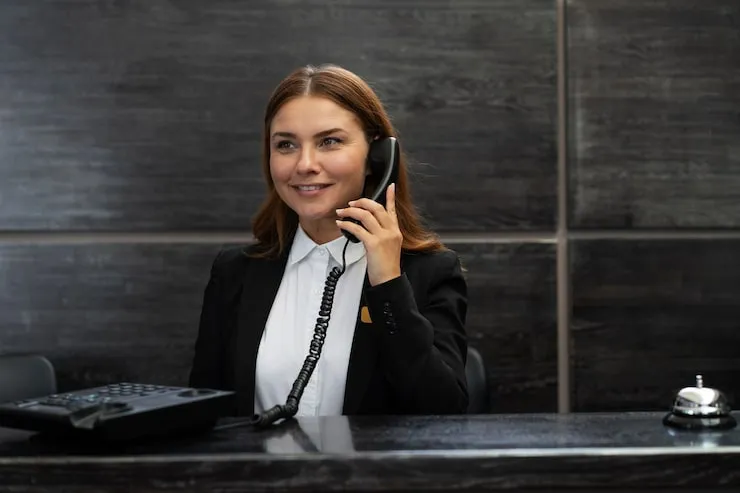 recepcjonistka hotelowa z uśmiechem, obsługująca komputer i telefon